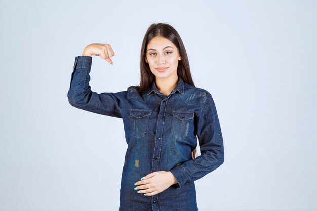 Jeune femme en chemise en jean montrant ses muscles du bras