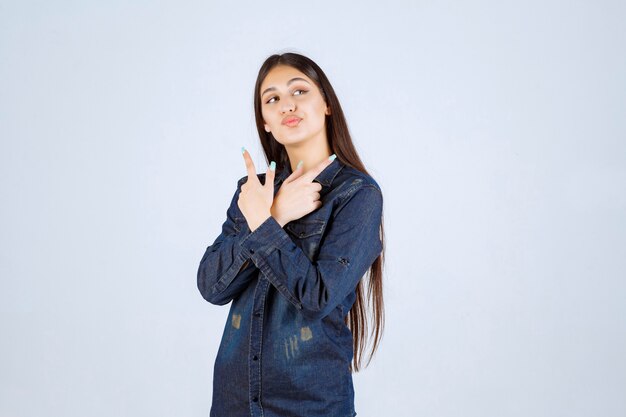 Jeune femme en chemise en jean pointant des deux côtés