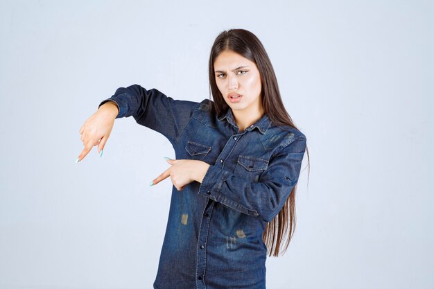 Jeune femme en chemise en jean pointant vers le bas