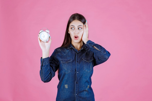 Jeune femme en chemise en jean tenant le réveil et couvrant son oreille à cause de la bague