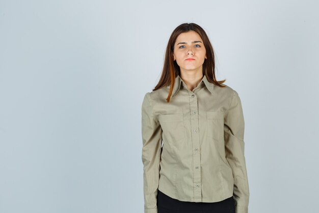 Jeune femme en chemise, jupe pinçant les lèvres et semblant nerveuse, vue de face.