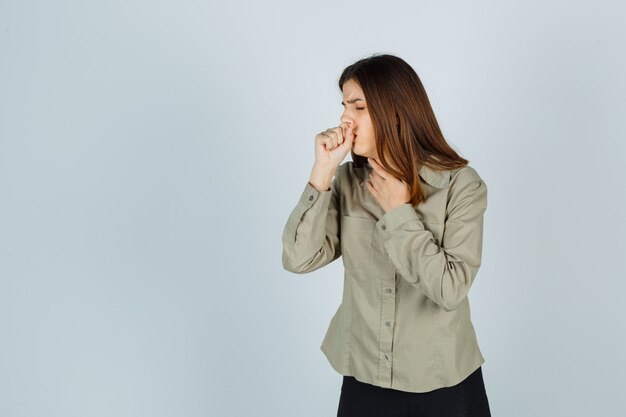 Jeune femme en chemise, jupe souffrant de toux et ayant l'air malade, vue de face.