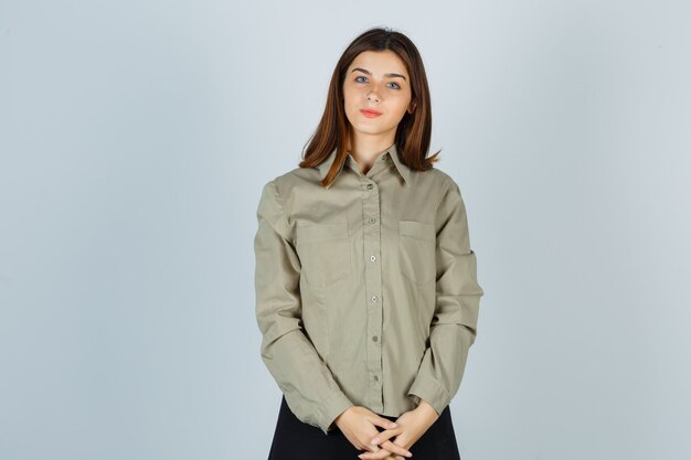 Jeune femme en chemise, jupe tenant la main devant elle et l'air positif, vue de face.