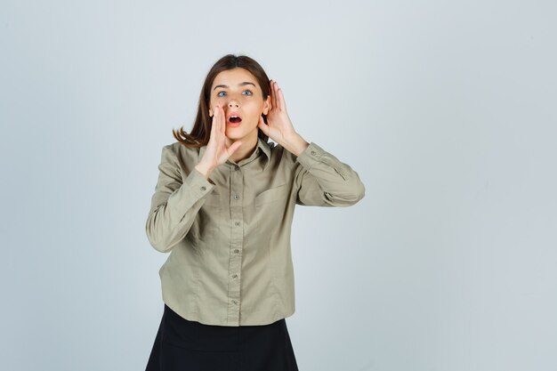 Jeune femme en chemise, jupe tenant les mains derrière l'oreille et près de la bouche pour dire le secret