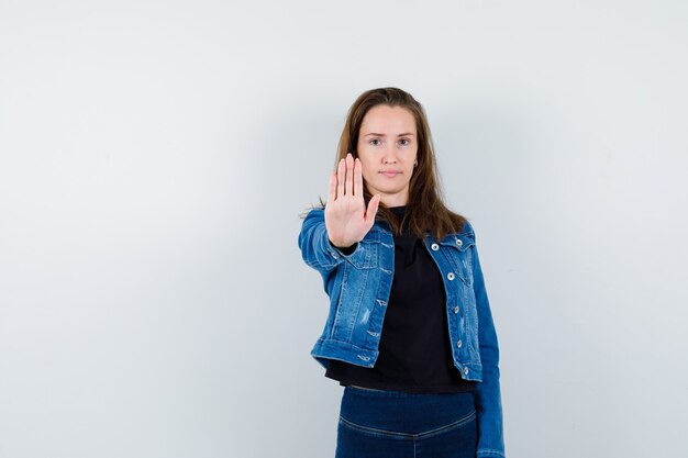 Jeune femme en chemise montrant un geste d'arrêt et l'air confiant, vue de face.