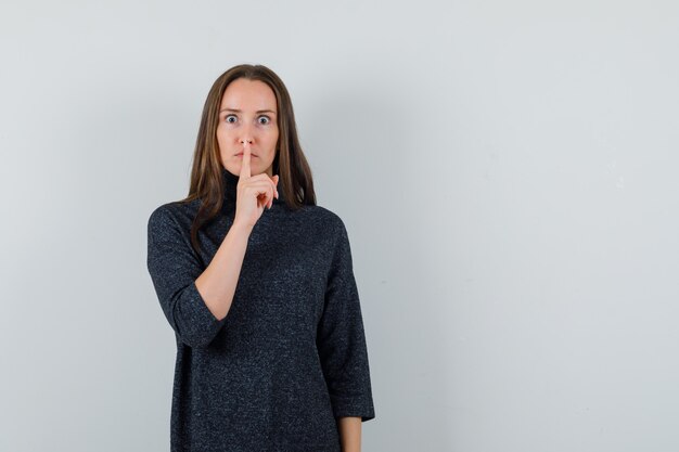 Jeune femme en chemise montrant le geste de silence et à la sérieuse