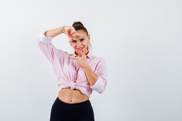 Jeune femme en chemise, pantalon faisant le geste du cadre et à la joyeuse vue de face.