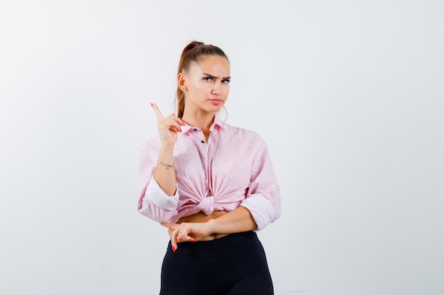 Photo gratuite jeune femme en chemise, pantalon pointant vers le haut, ayant une excellente idée ou solution et à la recherche intelligente, vue de face.