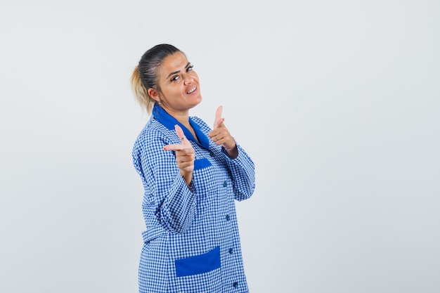 Jeune femme en chemise de pyjama vichy bleu pointant avec l'index et à la jolie vue de face.
