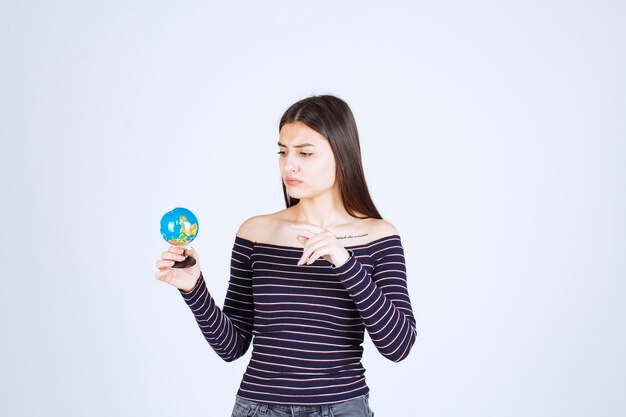 Jeune femme en chemise rayée tenant un mini globe et deviner une place dessus