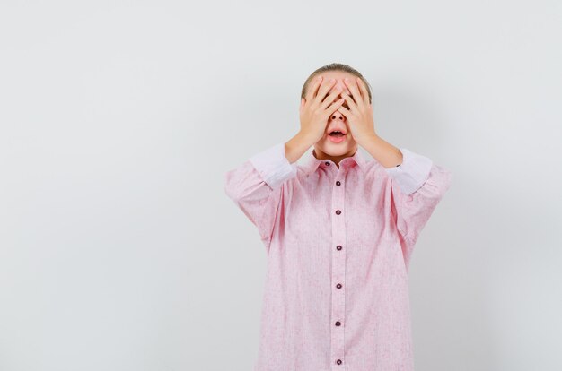 Jeune femme en chemise rose couvrant les yeux avec les mains et l'air excité