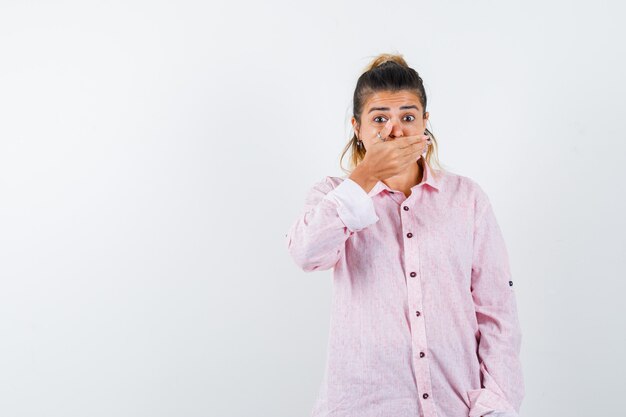 Jeune femme en chemise rose en gardant la main sur la bouche et à la peur