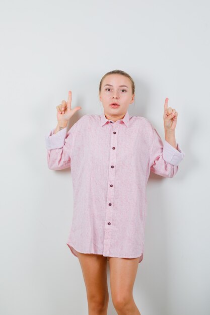 Jeune femme en chemise rose pointant vers le haut et à la confusion