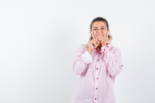 Jeune femme en chemise rose soutenant le menton sur les mains et à la recherche sensible