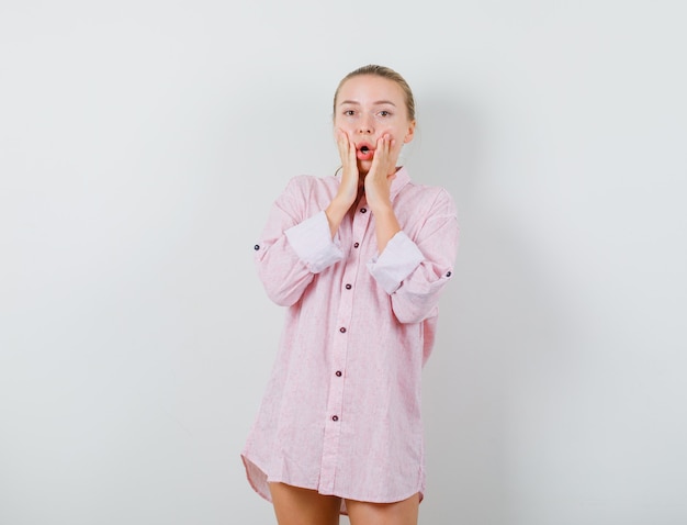 Jeune femme en chemise rose tenant les mains sur les joues et à la surprise