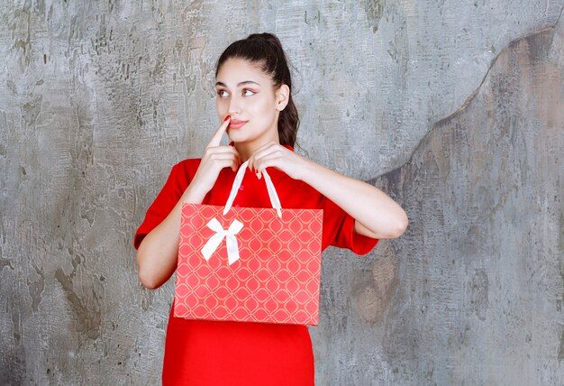 Jeune femme en chemise rouge tenant un sac à provisions rouge et a l'air confus et attentionné.