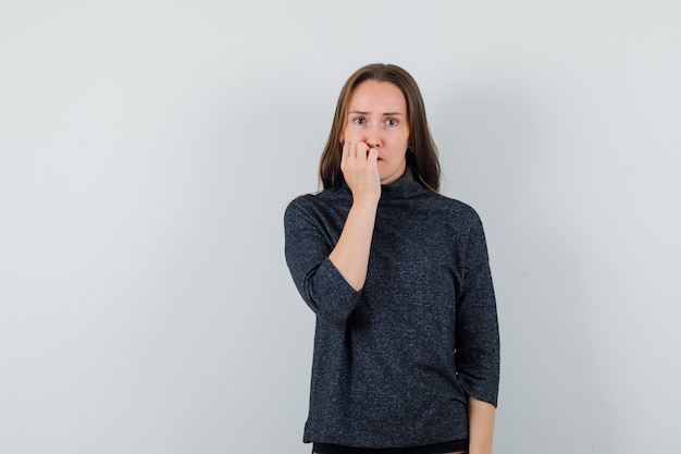 Jeune femme en chemise se ronger les ongles avec émotion et à la recherche d'anxiété