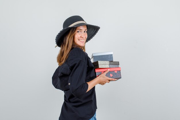 Jeune femme en chemise, short, chapeau tenant des coffrets cadeaux et à la bonne humeur.