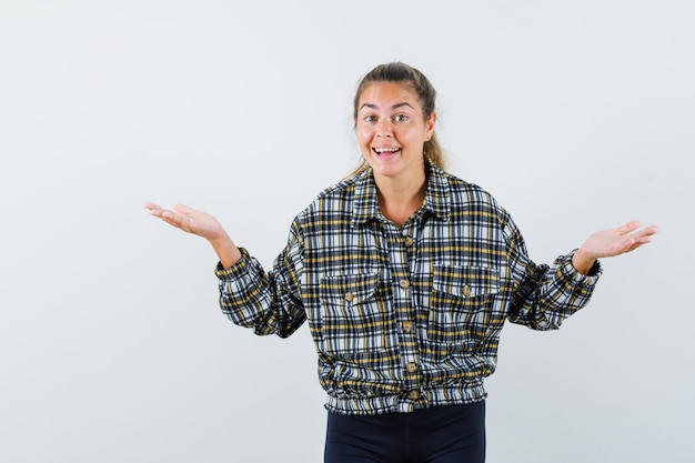 Jeune femme en chemise, short faisant le geste des échelles et l'air heureux, vue de face.