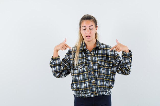 Jeune femme en chemise, short pointant vers le bas et regardant focalisée, vue de face.