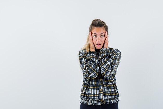 Jeune femme en chemise, short tenant les mains sur les joues et à la surprise, vue de face.