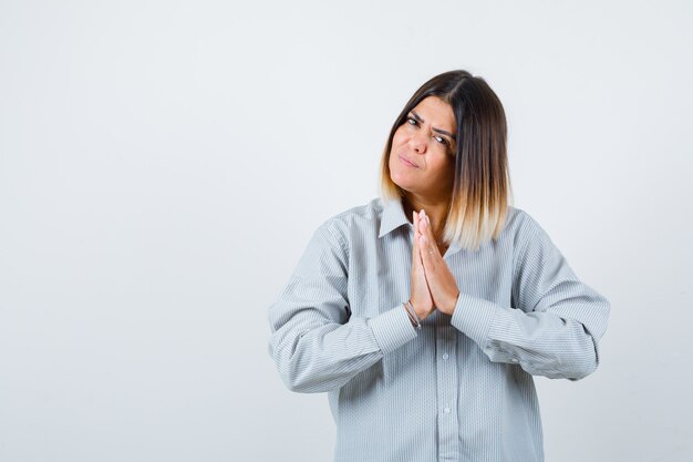 Jeune femme en chemise surdimensionnée montrant le geste de namaste et l'air paisible, vue de face.