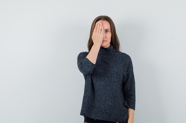 Jeune femme en chemise tenant la main sur les yeux et à la curiosité