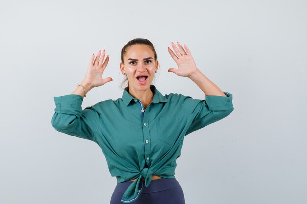 Jeune femme en chemise verte montrant un geste d'abandon et l'air choqué, vue de face.