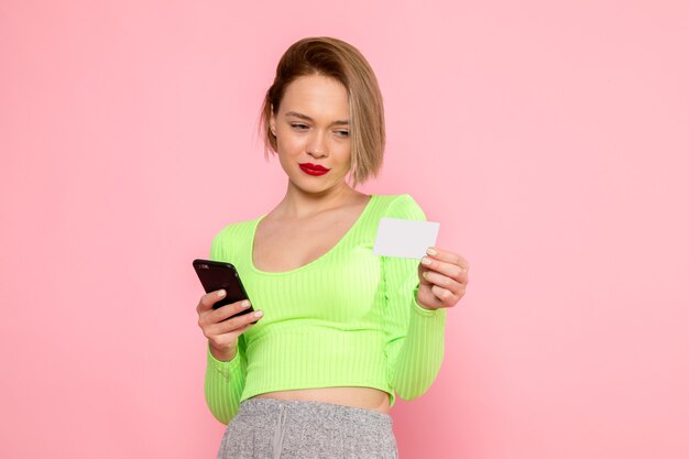 Jeune femme en chemise verte et pantalon gris à l'aide de téléphone et carte blanche