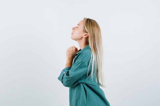 Jeune femme en chemise verte serrant les mains dans un geste de prière et à l'air plein d'espoir.