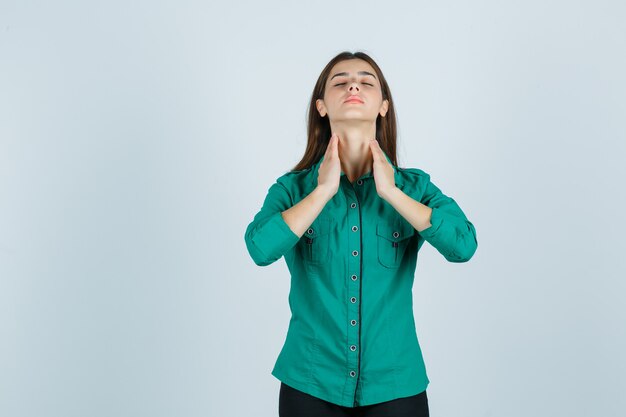 Jeune femme en chemise verte touchant la peau de son cou et à la vue de face, détendue.