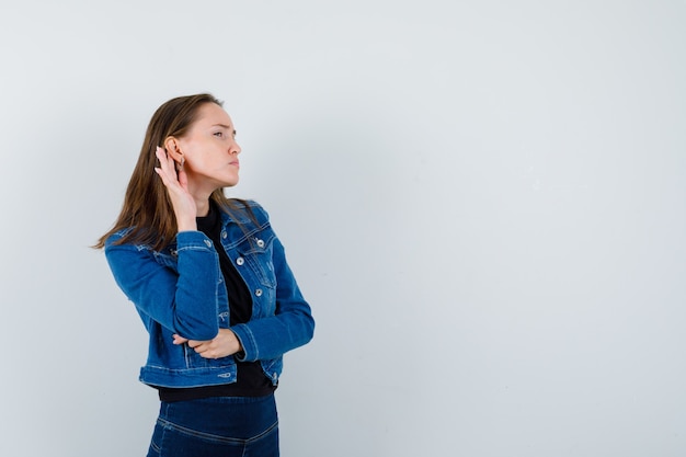 Jeune femme en chemise, veste entendant une conversation privée et l'air curieuse, vue de face.