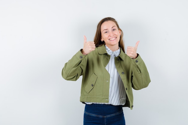 Jeune femme en chemise, veste montrant le double pouce vers le haut et l'air heureux, vue de face.