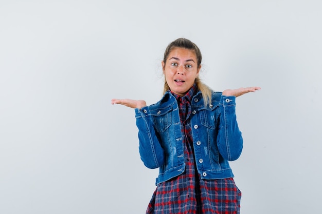 Jeune femme en chemise, veste montrant un geste impuissant et à la confusion, vue de face.