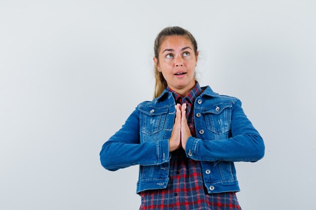 Jeune femme en chemise, veste montrant le geste de namaste et à la recherche d'espoir, vue de face.