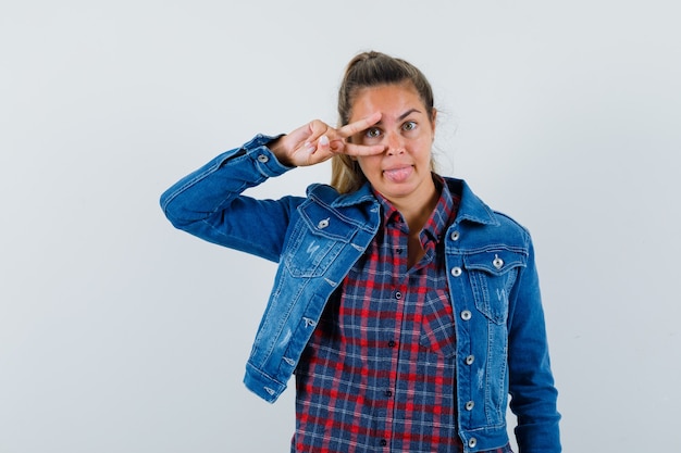 Jeune femme en chemise, veste montrant le signe V sur l'oeil et à la vue de face, heureux.