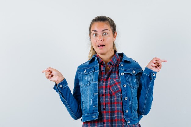 Jeune femme en chemise, veste pointant vers les deux côtés et regardant étonné, vue de face.