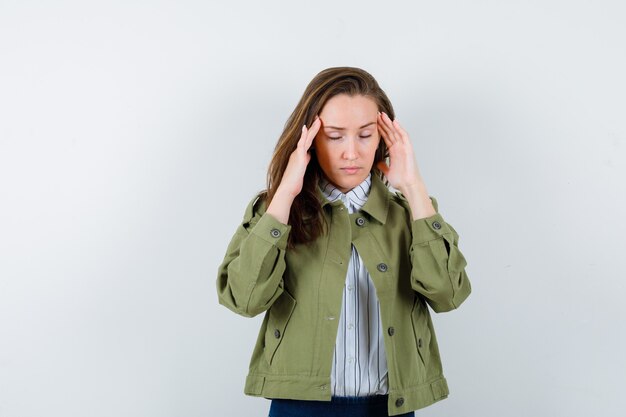 Jeune femme en chemise, veste se frottant les tempes, ayant mal à la tête et ayant l'air fatiguée, vue de face.