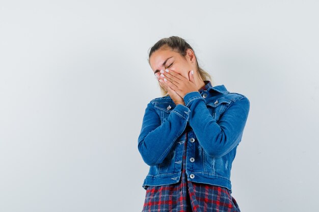 Jeune femme en chemise, veste tenant les mains sur la bouche et à la rêveuse, vue de face.