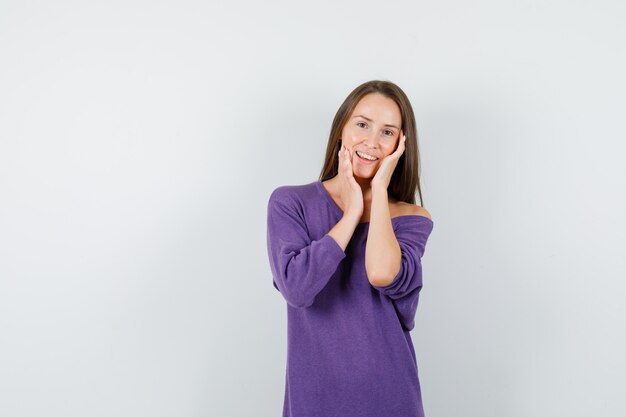 Jeune femme en chemise violette touchant son visage et à la charmante, vue de face.