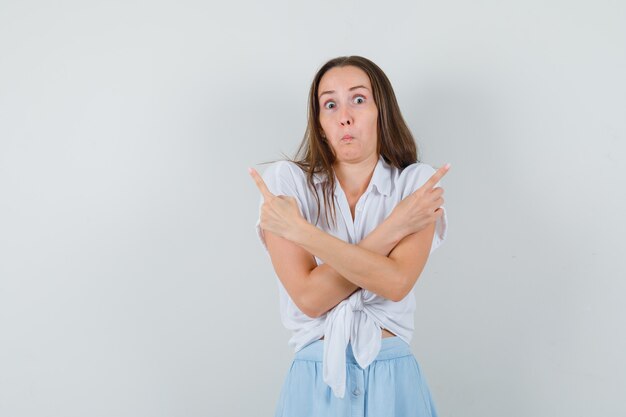 Jeune femme en chemisier blanc et jupe bleu clair pointant dans des directions opposées avec l'index et à la bonne humeur