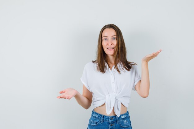 Jeune femme en chemisier blanc montrant un geste impuissant et à la recherche d'espoir, vue de face.