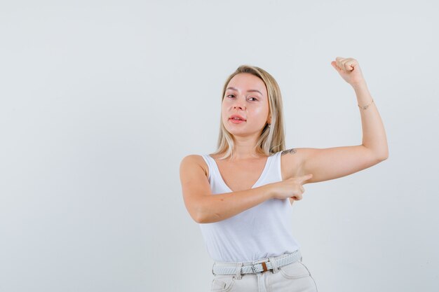 Jeune femme en chemisier blanc pointant sur les muscles de ses bras et à la recherche