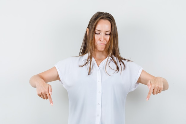 Photo gratuite jeune femme en chemisier blanc pointant vers le bas et à la recherche de stress