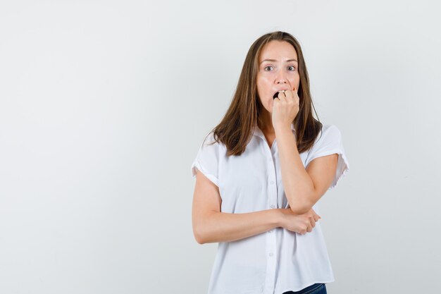 Jeune femme en chemisier blanc tenant le poing sur sa bouche et l'air inquiet