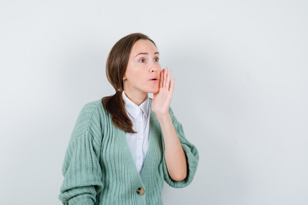 Jeune femme en chemisier, cardigan gardant la main près de la bouche, détournant les yeux et l'air concentré, vue de face.