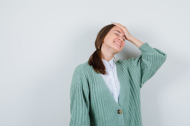 Jeune femme en chemisier, cardigan avec la main sur la tête et à la gaieté, vue de face.