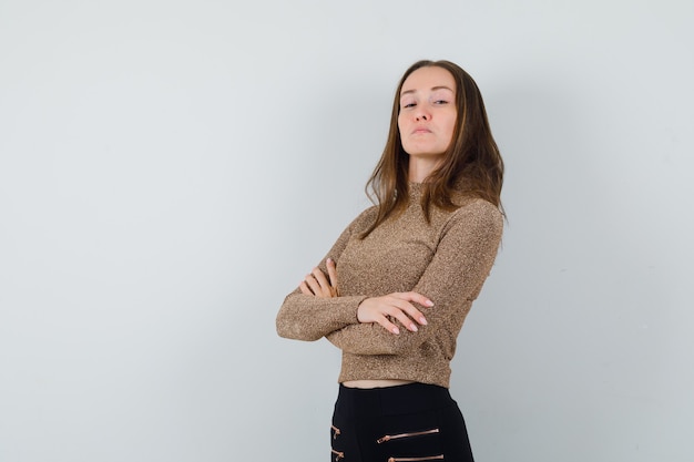 Jeune femme en chemisier doré debout avec les bras croisés et à la recherche de sérieux