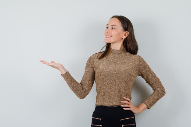 Jeune femme en chemisier doré étalant la paume de côté et à la joyeuse vue de face.