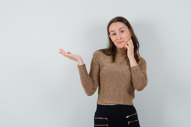 Jeune femme en chemisier doré étendant sa paume ouverte sur le côté, vue de face.